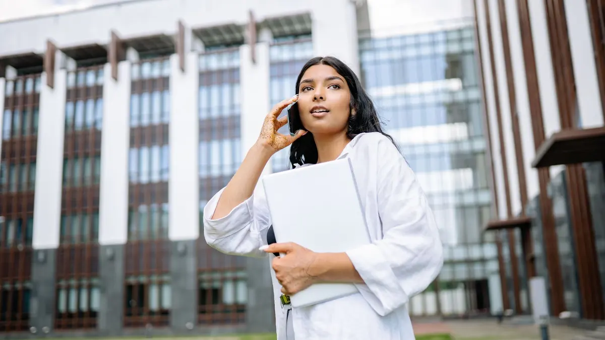 A young graduate carrying a laptop outside a modern office building, representing post-study work in New Zealand