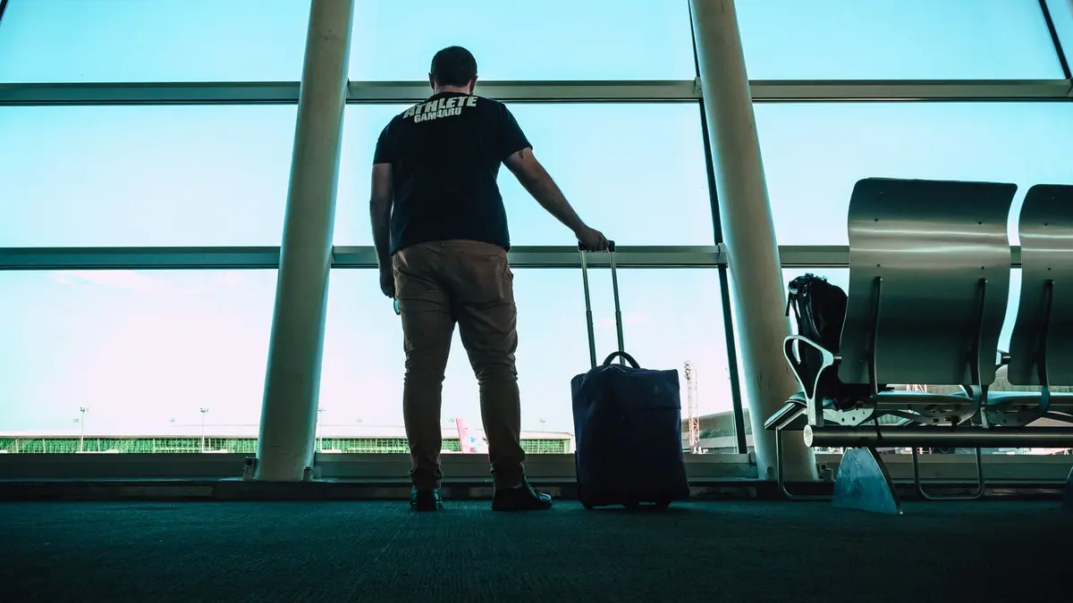 A student with a suitcase at an airport departure window watching planes, ready to travel to study in New Zealand